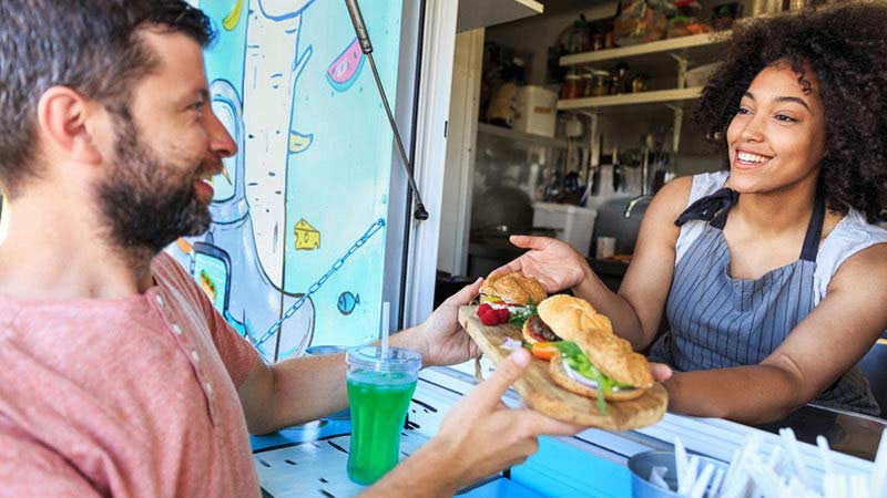 Man ordering hamburger from woman in food truck.